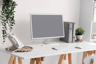 Blank computer monitor with telephone on table in light office