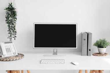 Blank computer monitor with telephone on table in light office