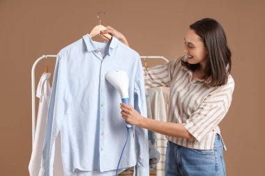 Güzel, genç bir kadın. Kahverengi arka planda modern buharlı giysiler.