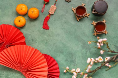 Frame made of mandarins with sakura, cups of tea and Chinese symbols on grey background. New Year celebration