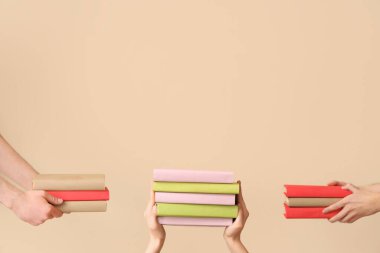 Hands holding stacks of books on beige background