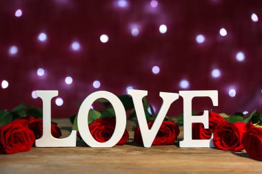 Red roses and word LOVE on wooden table