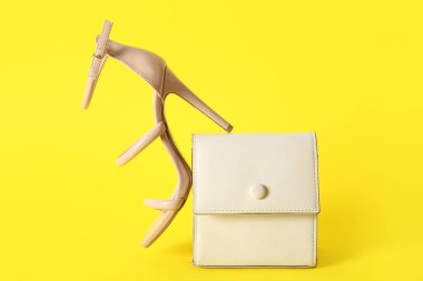Stylish high-heeled shoe and handbag on yellow background