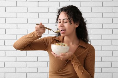 Beautiful young woman eating tasty cereal rings near light brick wall