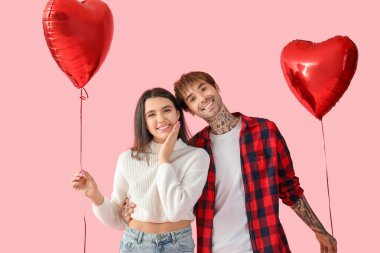 Young couple with heart-shaped air balloons for Valentine's day on pink background