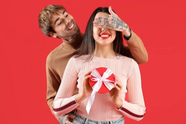 Young man greeting his beloved girlfriend with Valentine's day on red background