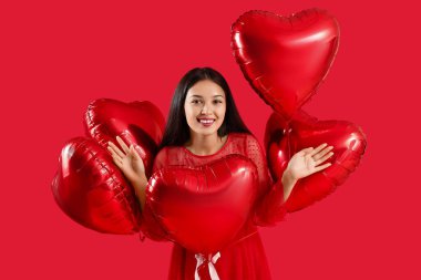 Young Asian woman with heart-shaped air balloons for Valentine's day on red background