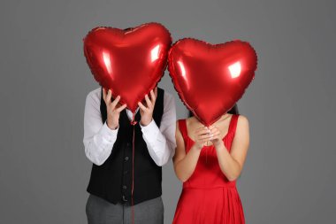 Couple with heart-shaped air balloons for Valentine's day on grey background