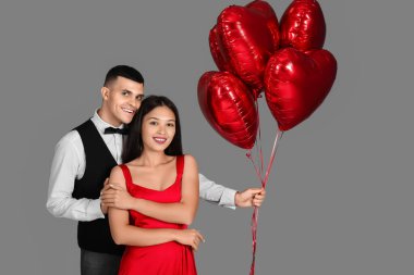 Young couple with heart-shaped air balloons for Valentine's day on grey background