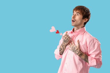 Funny young man with paper hearts on blue background. Valentine's day celebration