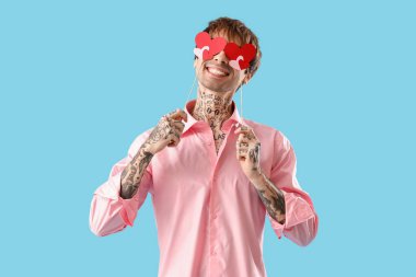 Funny young man with paper hearts on blue background. Valentine's day celebration