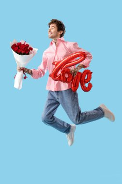 Jumping young man with bouquet of roses and air balloon in shape of word LOVE on blue background. Valentine's day celebration