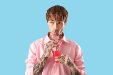 Handsome young man with tasty cocktail on blue background. Valentine's day celebration