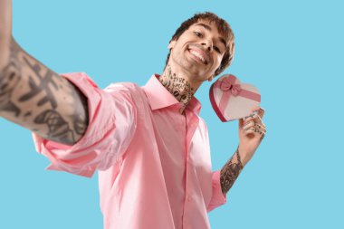 Handsome young man with gift for Valentine's day on blue background