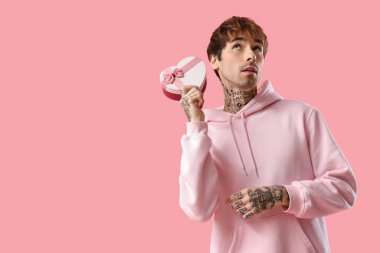 Handsome young man with gift box for Valentine's day on pink background