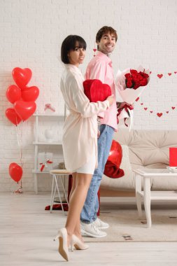 Young couple with bouquet of roses and gift for Valentine's day at home