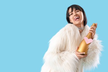 Funny young woman with bottle of champagne on blue background. Valentine's day celebration