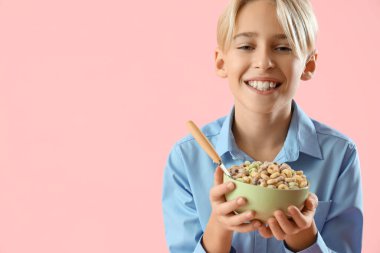 Happy little boy holding bowl with cereal rings on pink background