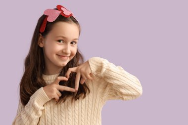 Cute little girl making heart with hands on lilac background. Valentine's day celebration