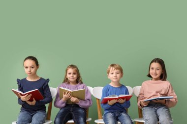 Little children reading books while sitting on chairs against green background