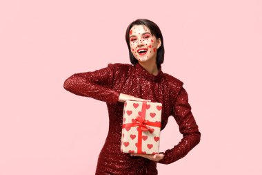 Beautiful young woman with creative makeup and gift for Valentines Day on pink background