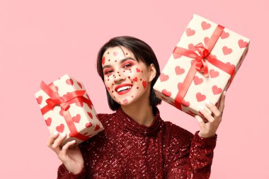 Beautiful young woman with creative makeup and gifts for Valentines Day on pink background