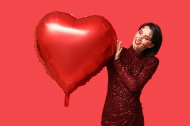 Beautiful young woman with creative makeup for Valentines Day and heart-shaped balloon on red background