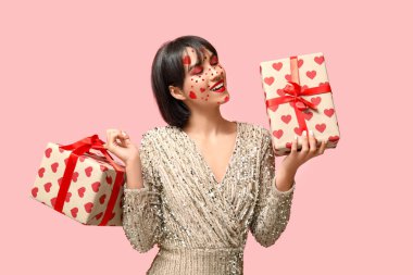 Beautiful young woman with creative makeup and gifts for Valentines Day on pink background