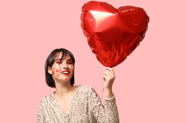 Beautiful young woman with creative makeup for Valentines Day and heart-shaped balloon on pink background