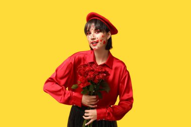 Beautiful young woman with creative makeup for Valentines Day and bouquet of roses on yellow background