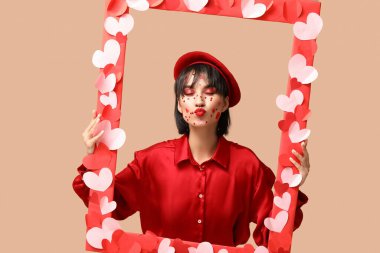 Beautiful young woman with creative makeup for Valentines Day and frame on beige background