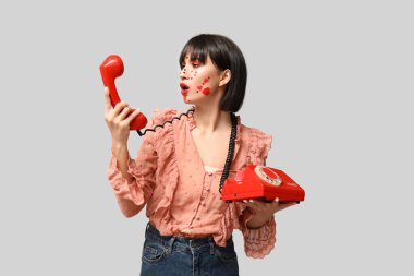 Beautiful young young woman with creative makeup for Valentines Day and retro telephone on grey background