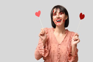 Beautiful young young woman with creative makeup for Valentines Day and hearts on grey background