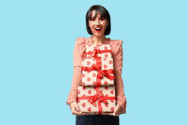 Beautiful young woman with creative makeup and gifts for Valentines Day on blue background