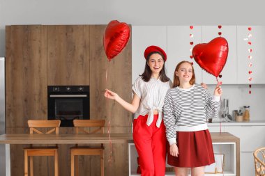 Young lesbian couple with heart-shaped balloons in kitchen on Valentine's Day