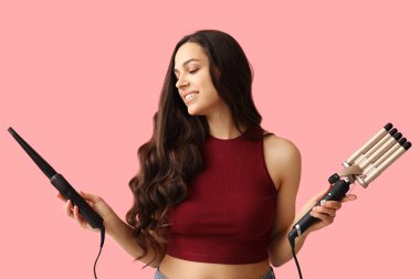 Beautiful young woman with different curling irons on pink background