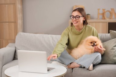 Young woman with cute Pomeranian dog and laptop sitting at home