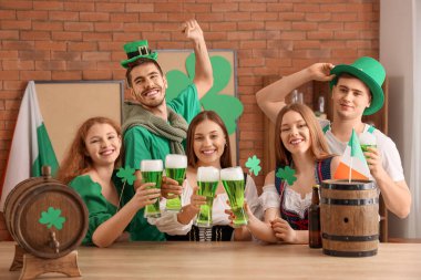 Group of young friends with beer celebrating St. Patrick's Day at table in pub