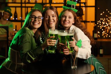Female friends with beer celebrating St. Patrick's Day in pub at night