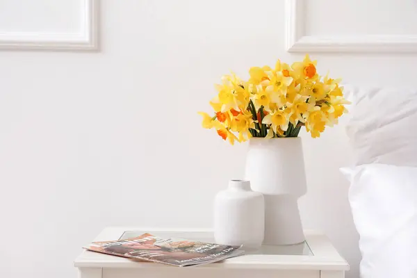 Vase with beautiful narcissus flowers and magazine on bedside table, closeup