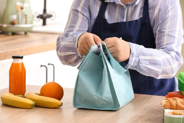 Mother packing meal for school lunch on table in kitchen