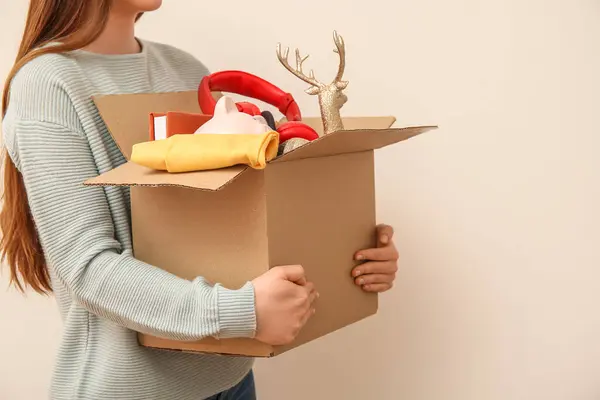 Woman holding box of unwanted stuff for yard sale on beige background