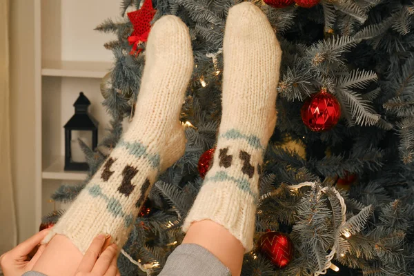Woman in warm socks at home near Christmas tree