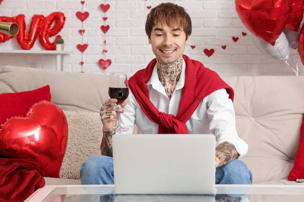 Handsome young man with glass of wine and laptop at home. Valentine's day celebration
