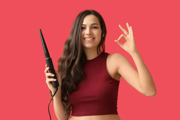 Beautiful Young Woman Curling Iron Showing Red Background — Stockfoto