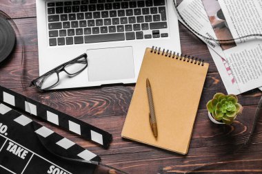 Dizüstü bilgisayarlı, gözlüklü ve siyah ahşap arka planda film alkışlı bir defter.