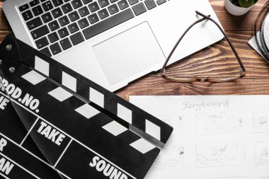 Ahşap arka planda film alkışları, dizüstü bilgisayar ve gözlüklü hikaye tahtası