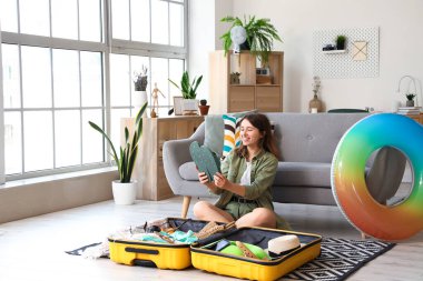 Evdeki bavuldan parmak arası terlikleri çıkaran genç bir kadın.