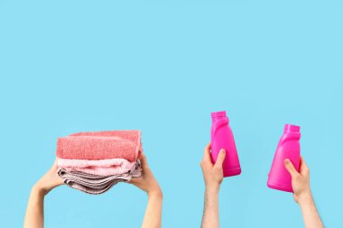 Çamaşır deterjanı şişeleri ve temiz havluları olan insanlar mavi arka planda.