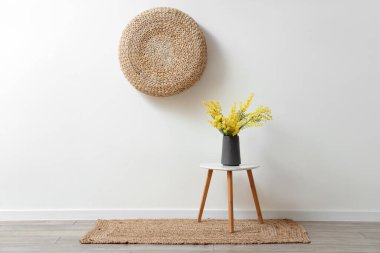 Beyaz duvarın yanındaki sehpanın üzerinde güzel mimoza çiçekleri olan vazo.